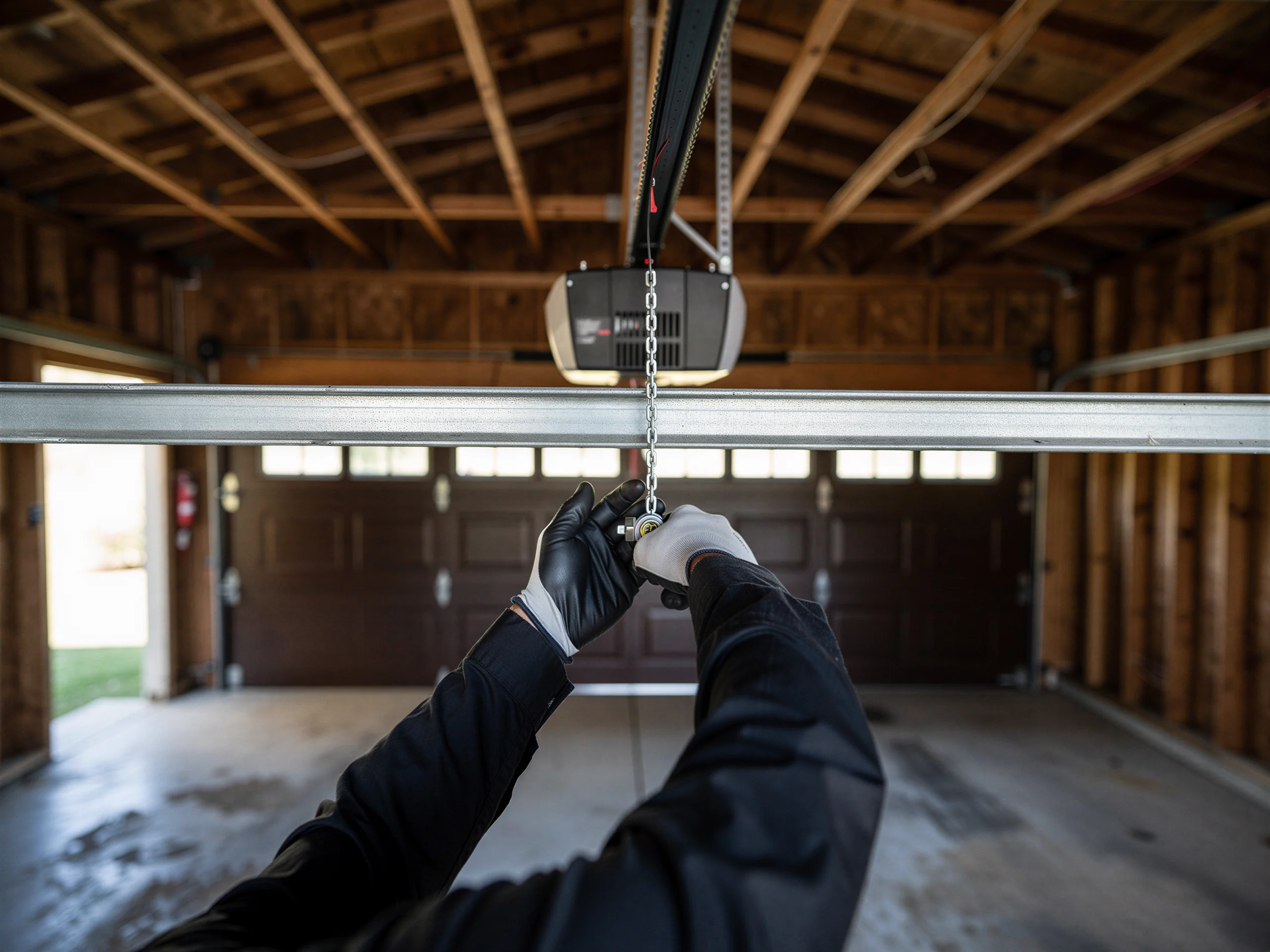 A technician in gloves adjusts a garage door opener chain.