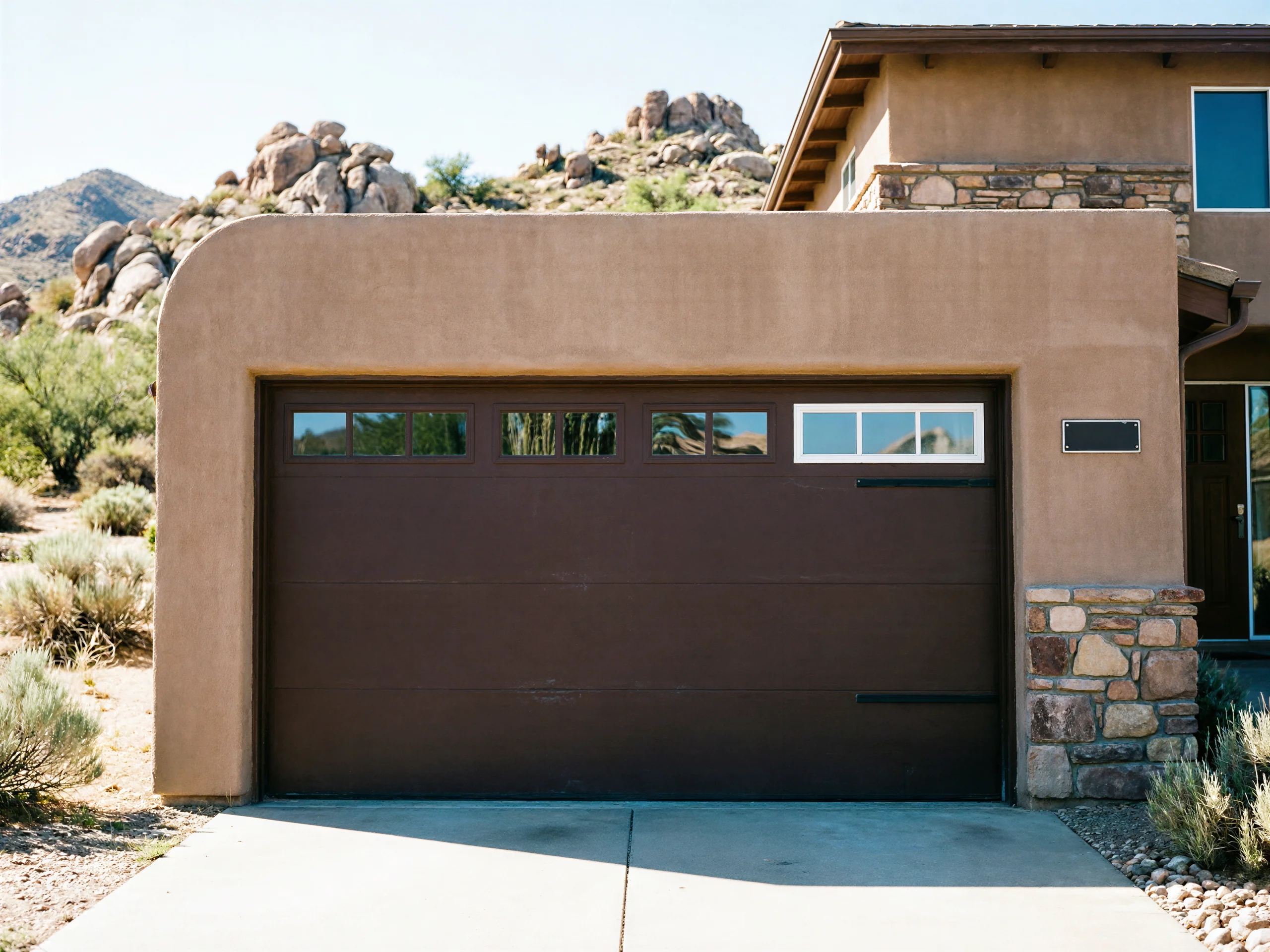 A brown garage door with windows is set in a stucco house.