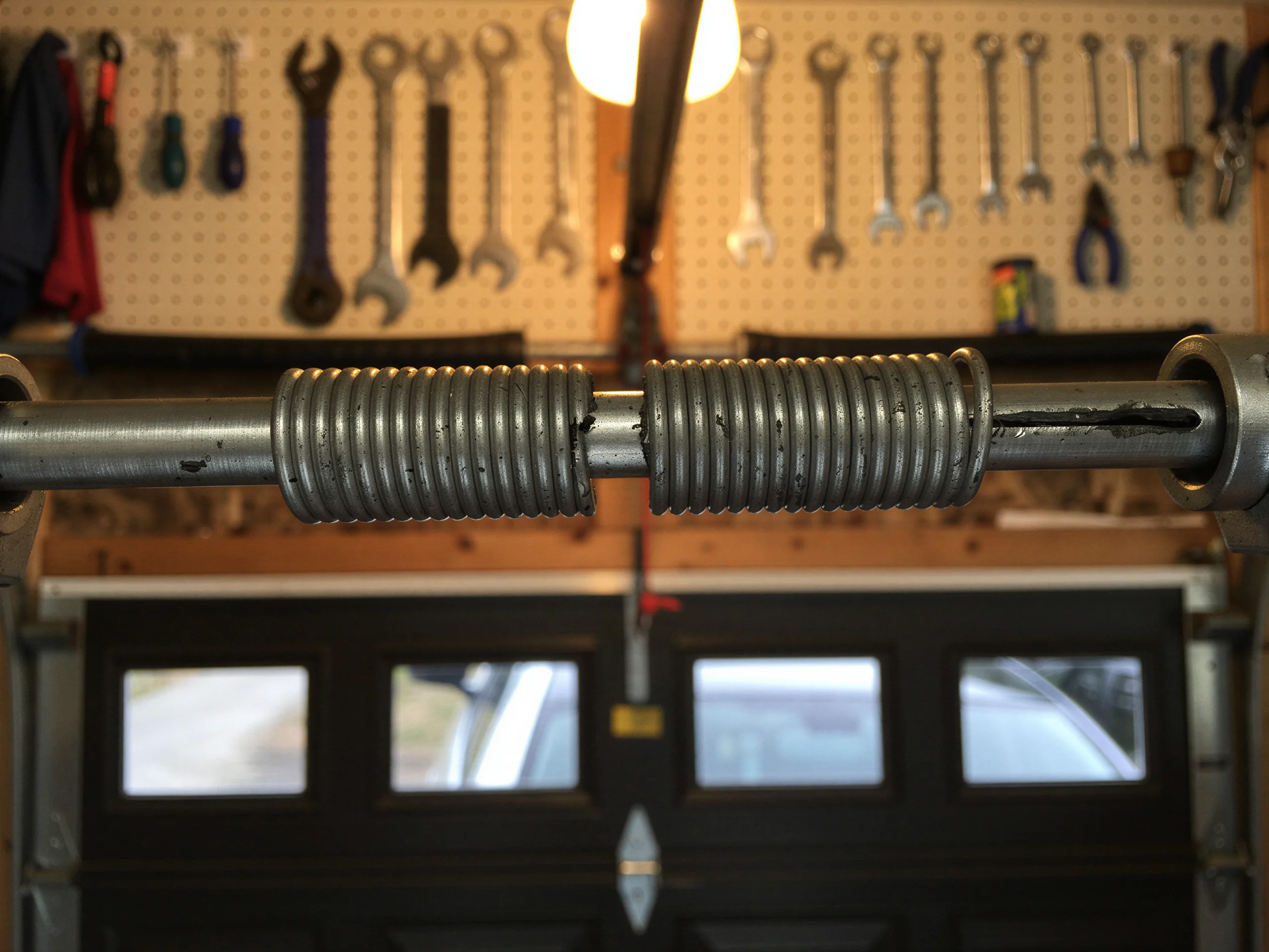 Two torsion springs are on a metal rod above a dark garage door.